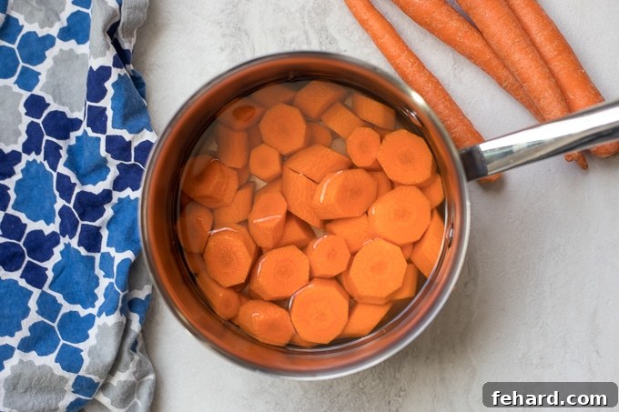 Quick & Sweet Glazed Carrots 5 A saucepan filled with sliced carrots covered with water, simmering on a stovetop.