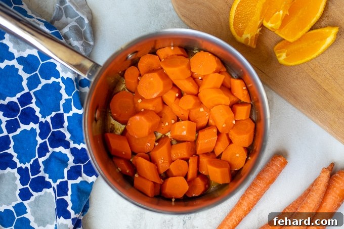 Quick & Sweet Glazed Carrots 6 A pan with cooked carrots coated in a glossy orange and maple glaze, with garlic visible, next to fresh oranges.