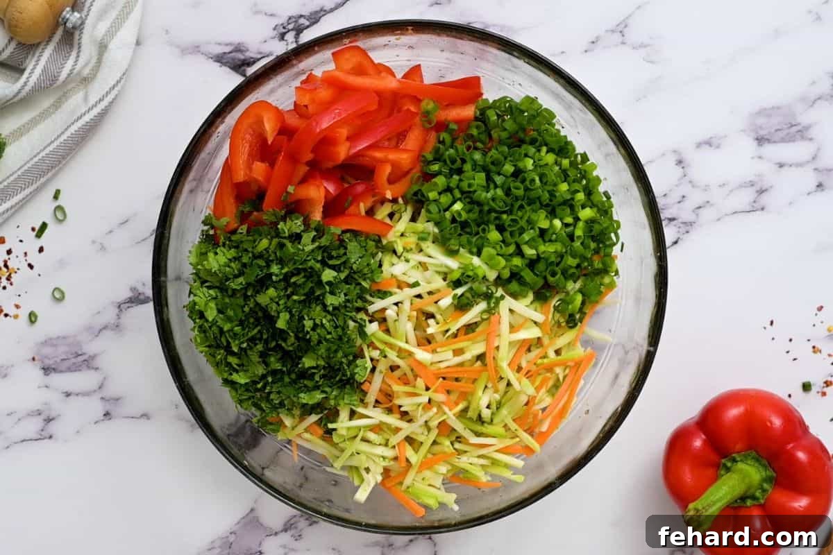 Cold Noodle Salad with Vegetables A clear glass bowl filled with noodles, broccoli slaw, fresh cilantro, green onions, and red bell pepper, tossed together.