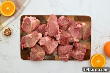 Pork shoulder roast cut in large chunks seasoned with salt and pepper on cutting board.