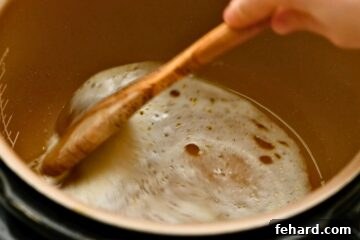 Wooden spoon scraping up browned bits off bottom of inner pot from searing pork roast.