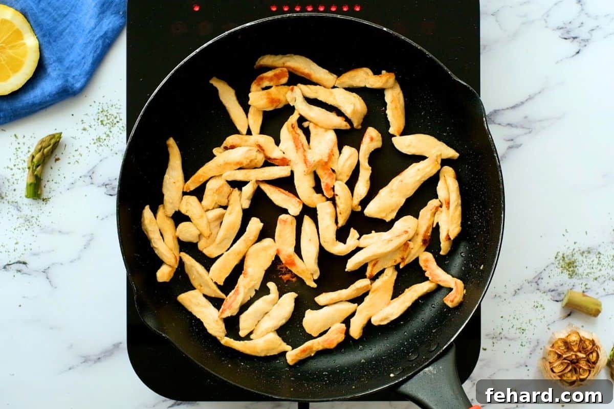 Thin slices of chicken browning in a hot saute pan in skillet.