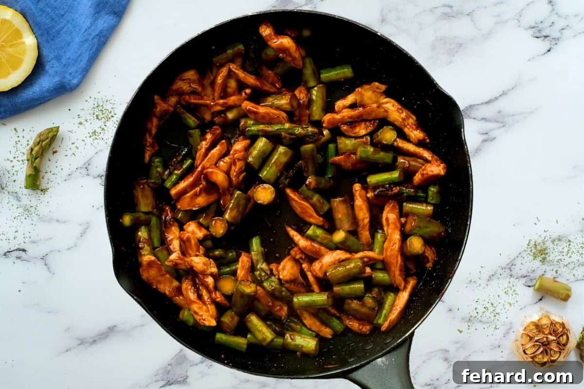 Chicken Asparagus with honey soy lemon stir fry sauce thickening in skillet.