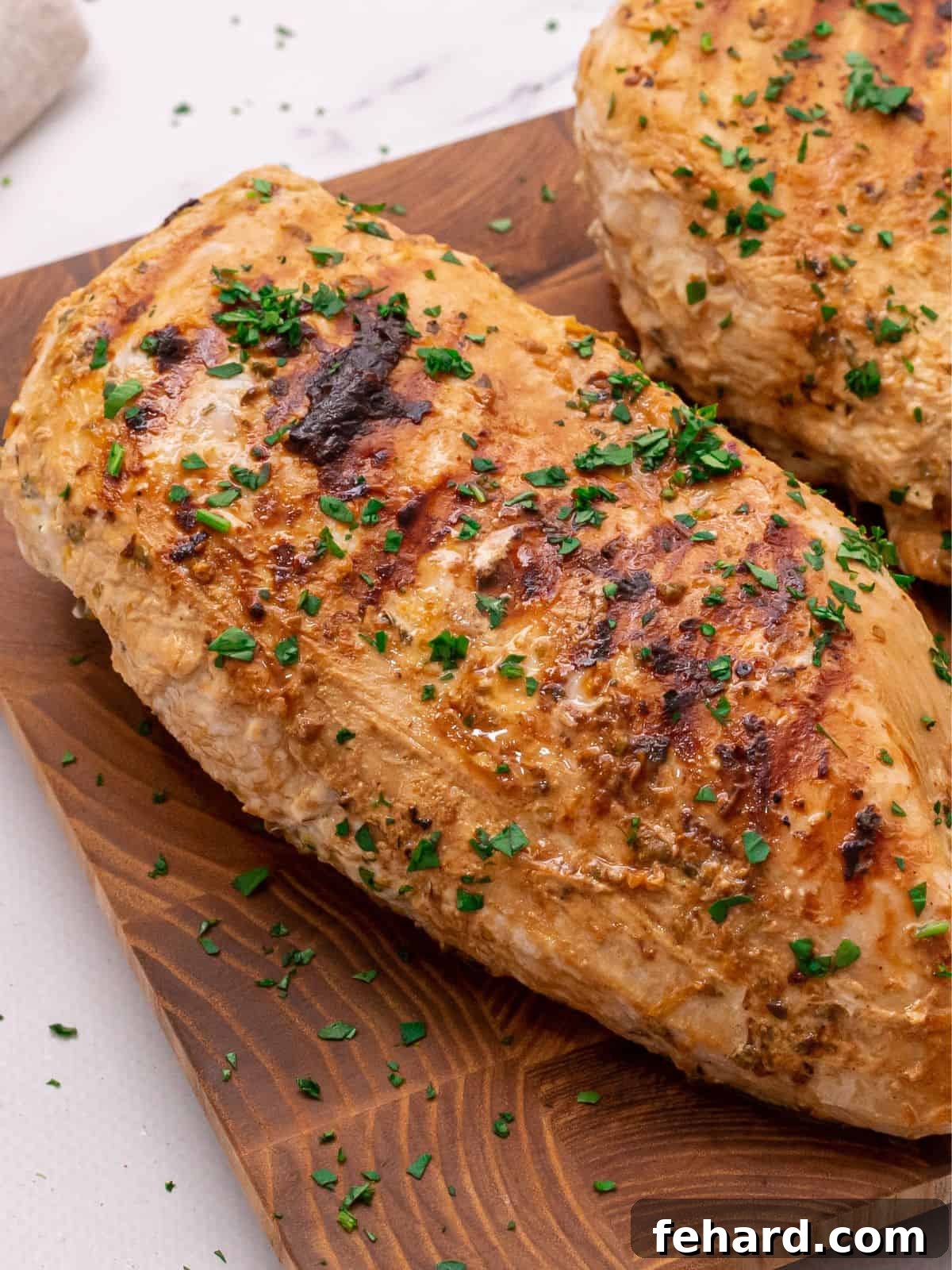 Cooked marinated Greek chicken on wooden cutting board topped with fresh parsley.