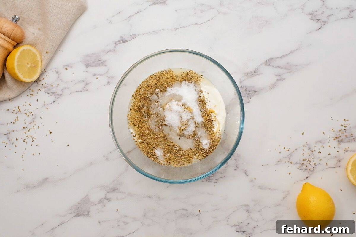 Greek yogurt, lemon juice, lemon zest, and salt in mixing bowl with whole lemons in background.