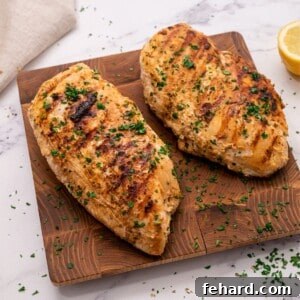 Cooked marinated Greek chicken on wooden cutting board topped with fresh parsley.