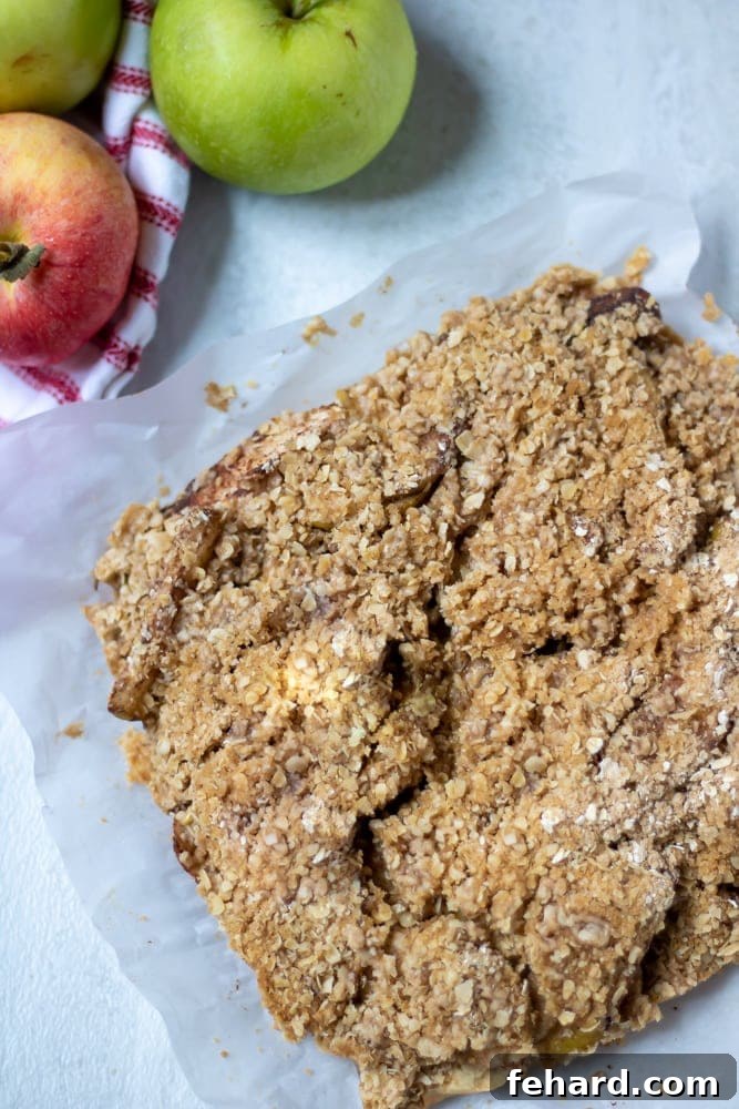 Baked Apple Pie Bars with Oat Crumble next to fresh apples, showcasing a perfect slice.