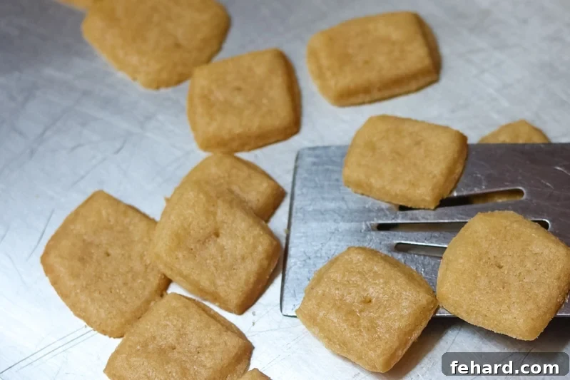 A metal spatula lifting a batch of freshly baked, golden-brown homemade cheese crackers off a baking sheet, showcasing their crisp texture.