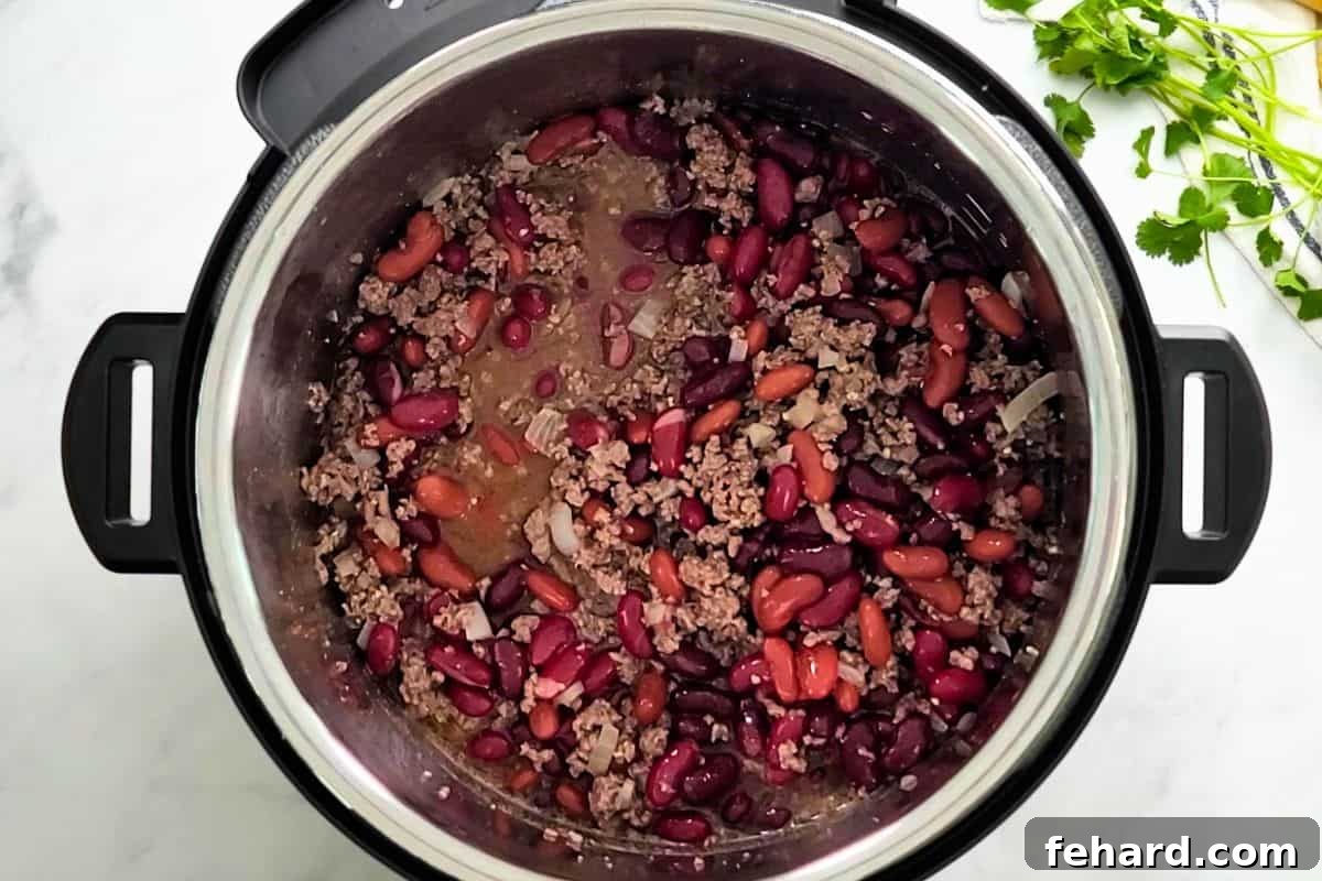 Adding Liquid and Beans to Instant Pot Chili Base Sauteed beef with beer, beef stock, and kidney beans mixed together inside Instant Pot.