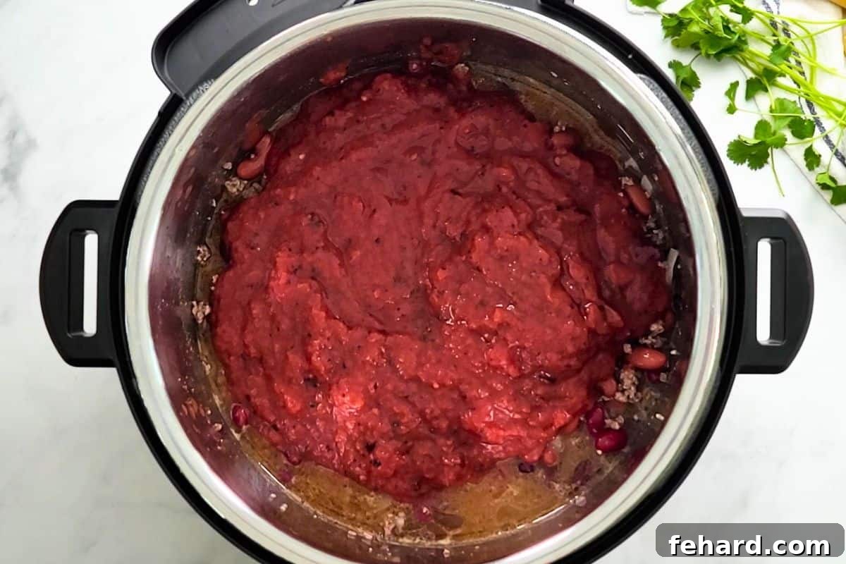 Tomatoes Layered on Top of Chili Ingredients for Pressure Cooking Instant Pot with beef and bean, beef broth, and crushed tomatoes layered on top.