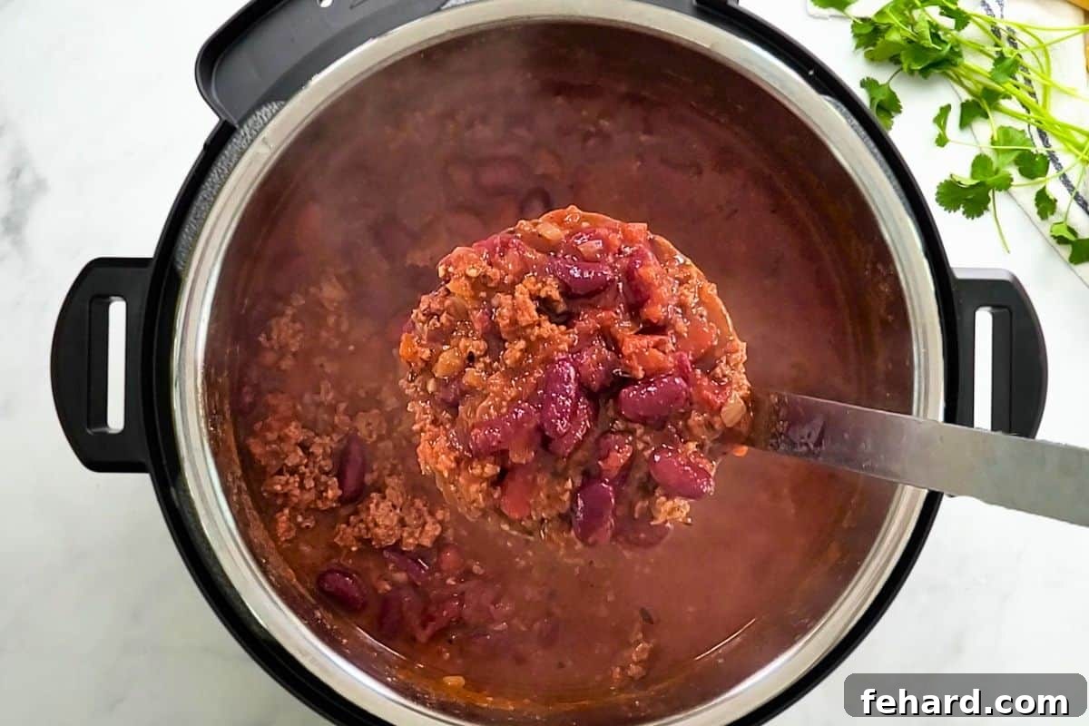 Serving Freshly Cooked Instant Pot Chili Scoop of Beef and Bean Instant Pot Chili being ladled out of Instant Pot.