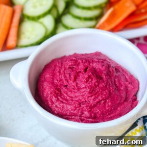Close up of a spoonful of vibrant roasted beet hummus, showcasing its creamy texture and rich pink color, with a slight garnish of fresh herbs.