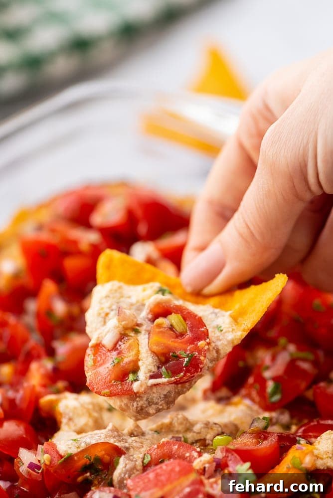Chip scooping up creamy refried bean taco dip, showcasing its layered goodness.