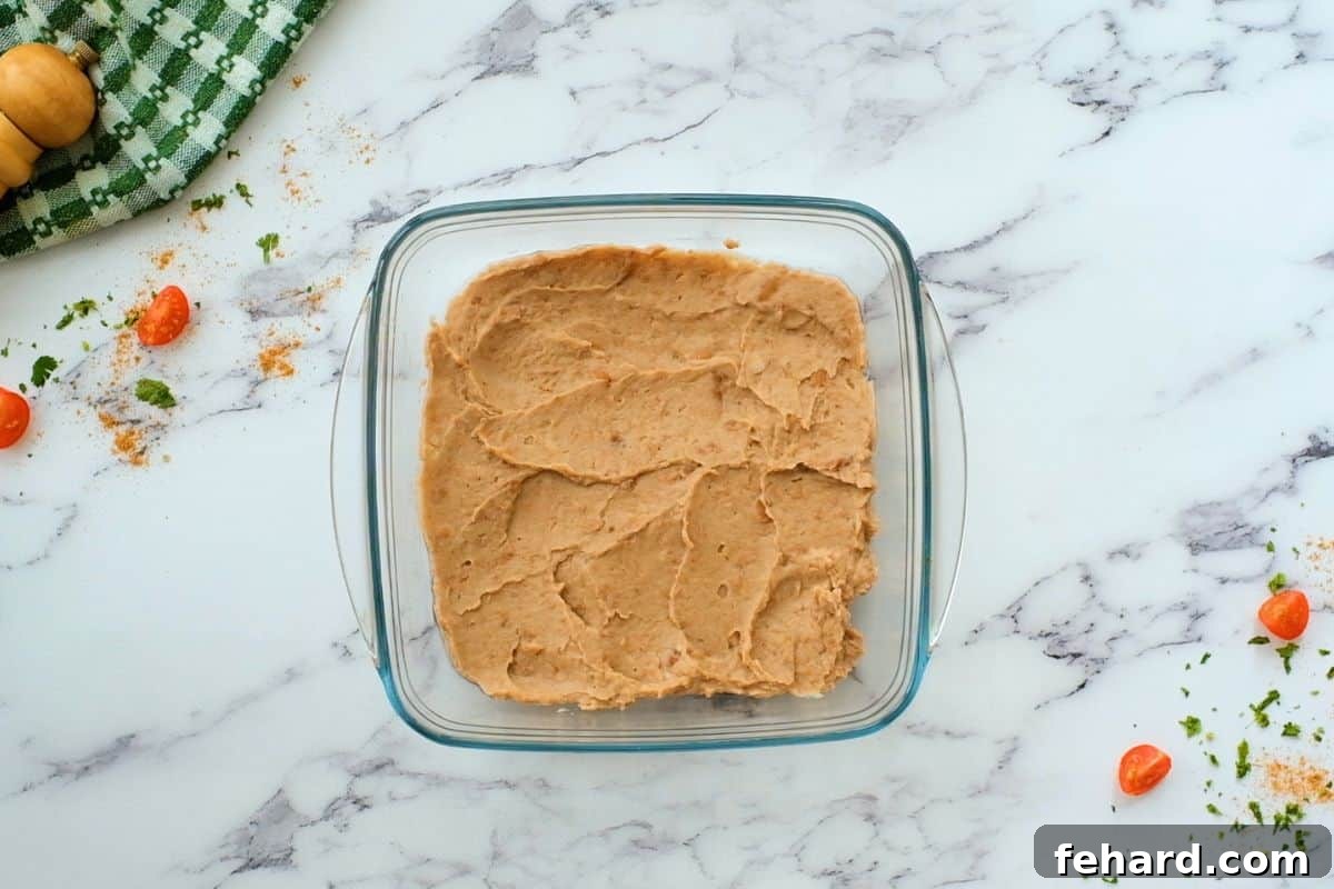 Refried beans spread in a baking dish, ready for the next layer.