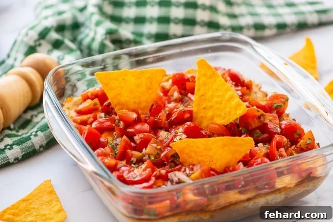 Glass dish filled with warm, creamy taco dip, garnished with fresh toppings and surrounded by tortilla chips.