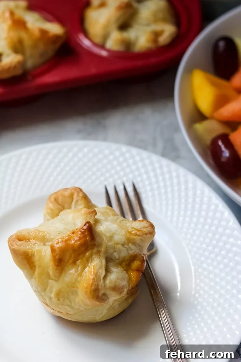 Puff pastry egg breakfast quiche on white plate with fruit.
