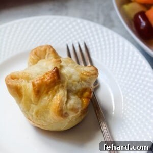 Puff Pastry mini quiche on plate with fork and fruit to side.