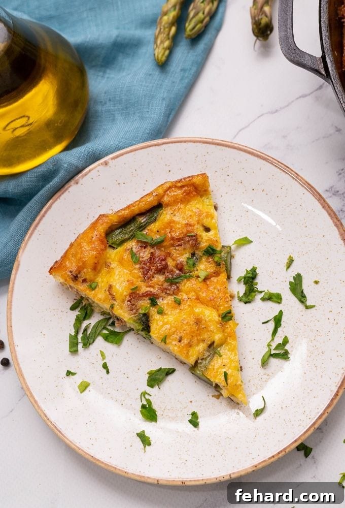 A perfectly cooked slice of Asparagus Frittata served on a pristine white plate, showcasing its fluffy texture, golden edges, and visible pieces of vibrant green asparagus and broccoli.