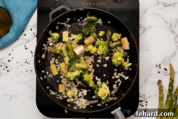 Broccoli, asparagus, and onions sautéing in a cast iron skillet.
