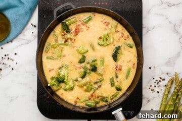 Bacon, vegetables, and eggs combined in an oven-safe skillet before baking.