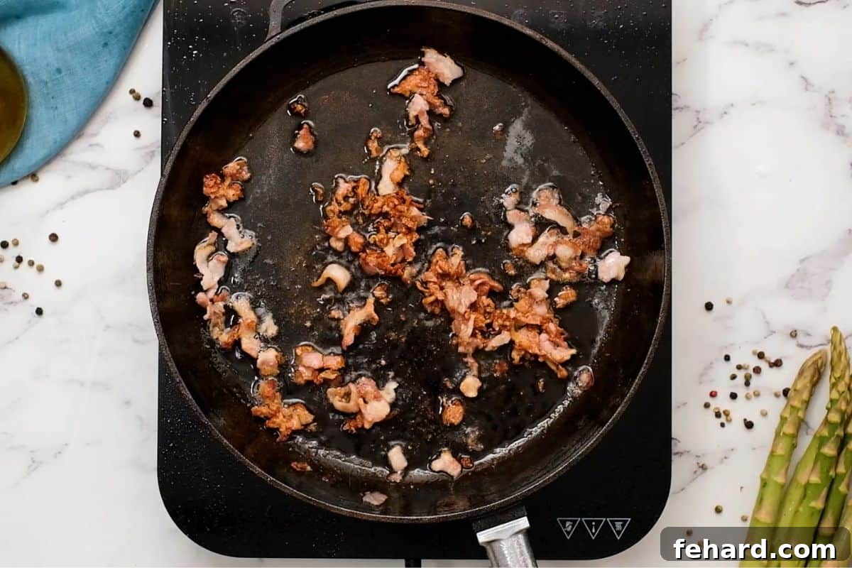 Crispy diced bacon rendered in a hot cast-iron skillet, with fresh asparagus spears visible nearby.