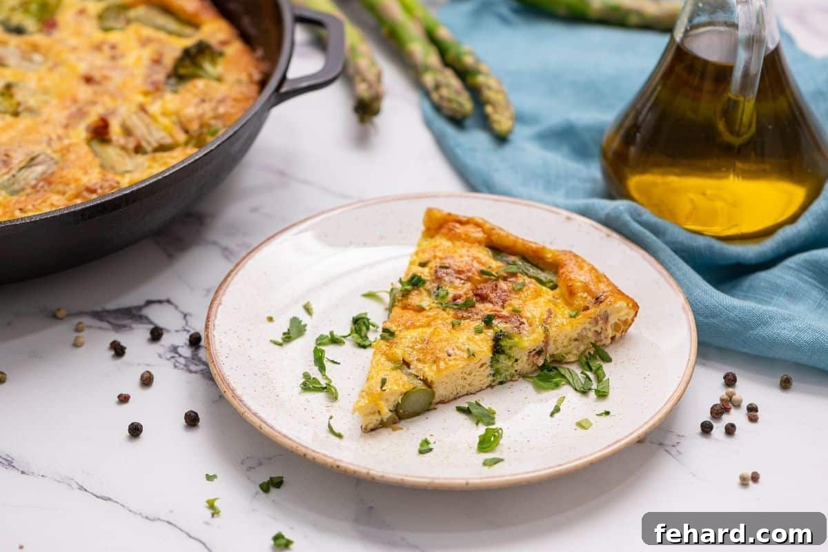 A beautifully presented slice of Asparagus Frittata on a white plate, placed next to the full frittata still in its cast-iron skillet, showcasing its vibrant ingredients and golden-brown top.