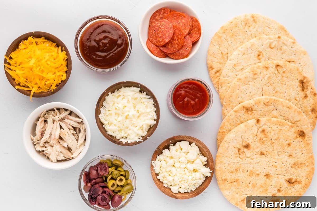 Various ingredients for a variety of pita bread pizzas, including different sauces, cheeses, and fresh vegetables, neatly arranged on a kitchen counter.