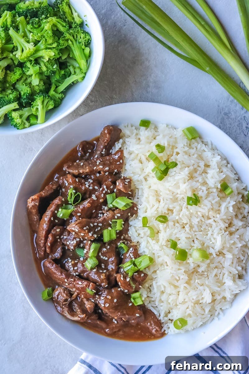 Instant Pot Mongolian Beef with Steamed Rice and Broccoli plated in a white bowl, garnished with green onions and sesame seeds.