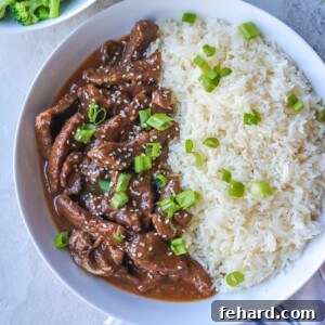 Instant Pot Mongolian Beef dished up in white serving platter with white rice, garnished with green onions.
