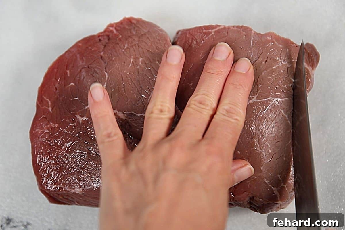Close-up shot showing how to cut beef against the grain with a sharp knife on a cutting board.