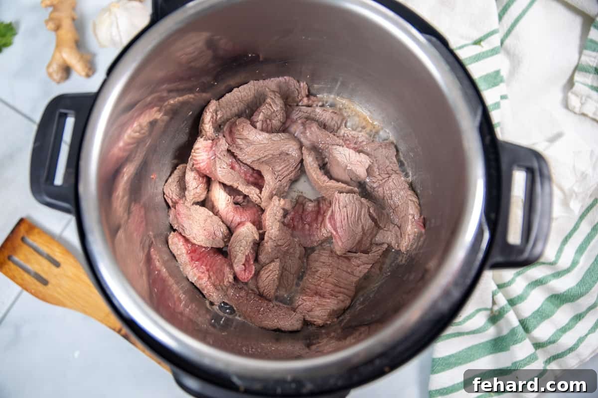 Seared beef strips browning in the inner pot of an Instant Pot.