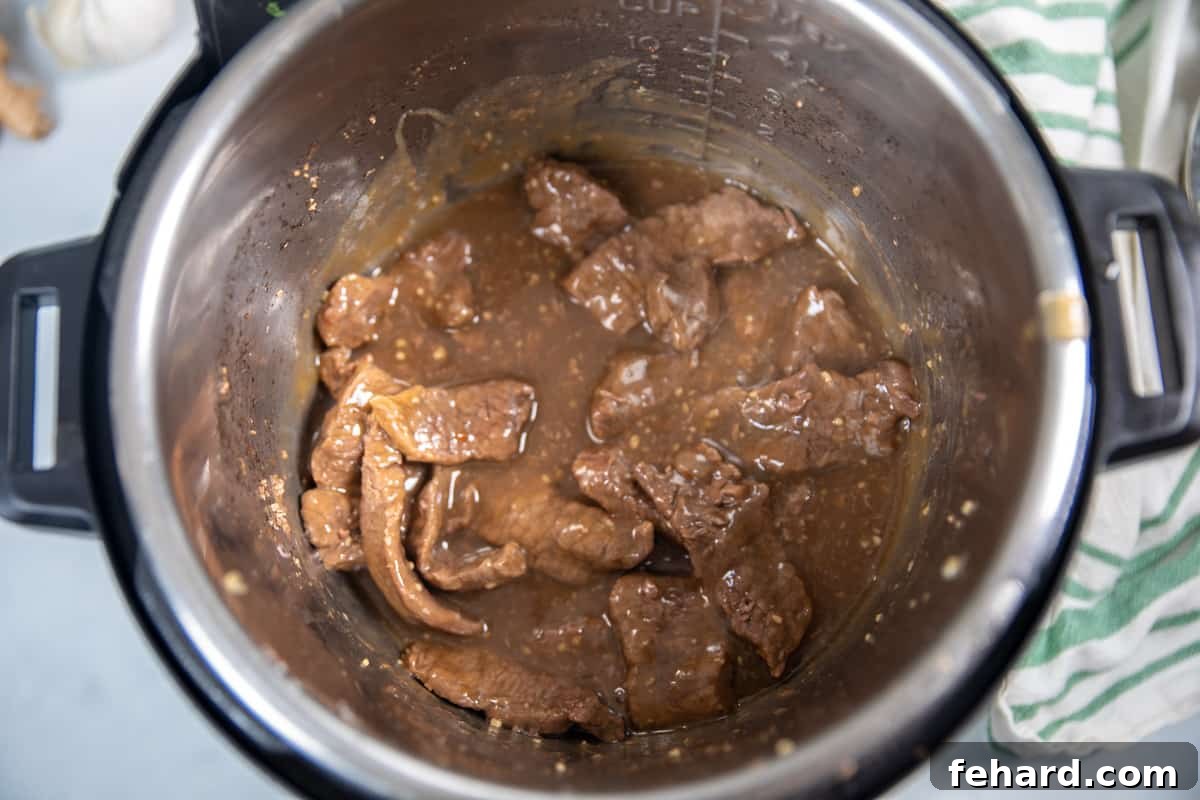 Close-up of thickened Mongolian sauce bubbling in the inner pot of an Instant Pot, coating the beef.