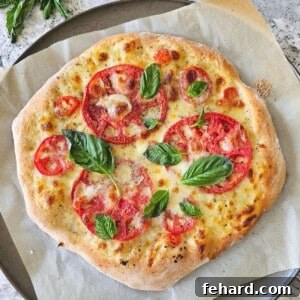 Baked tomato pizza topped with freshly grated parmesan cheese and fresh basil leaves on pizza pan topped with parchment paper.