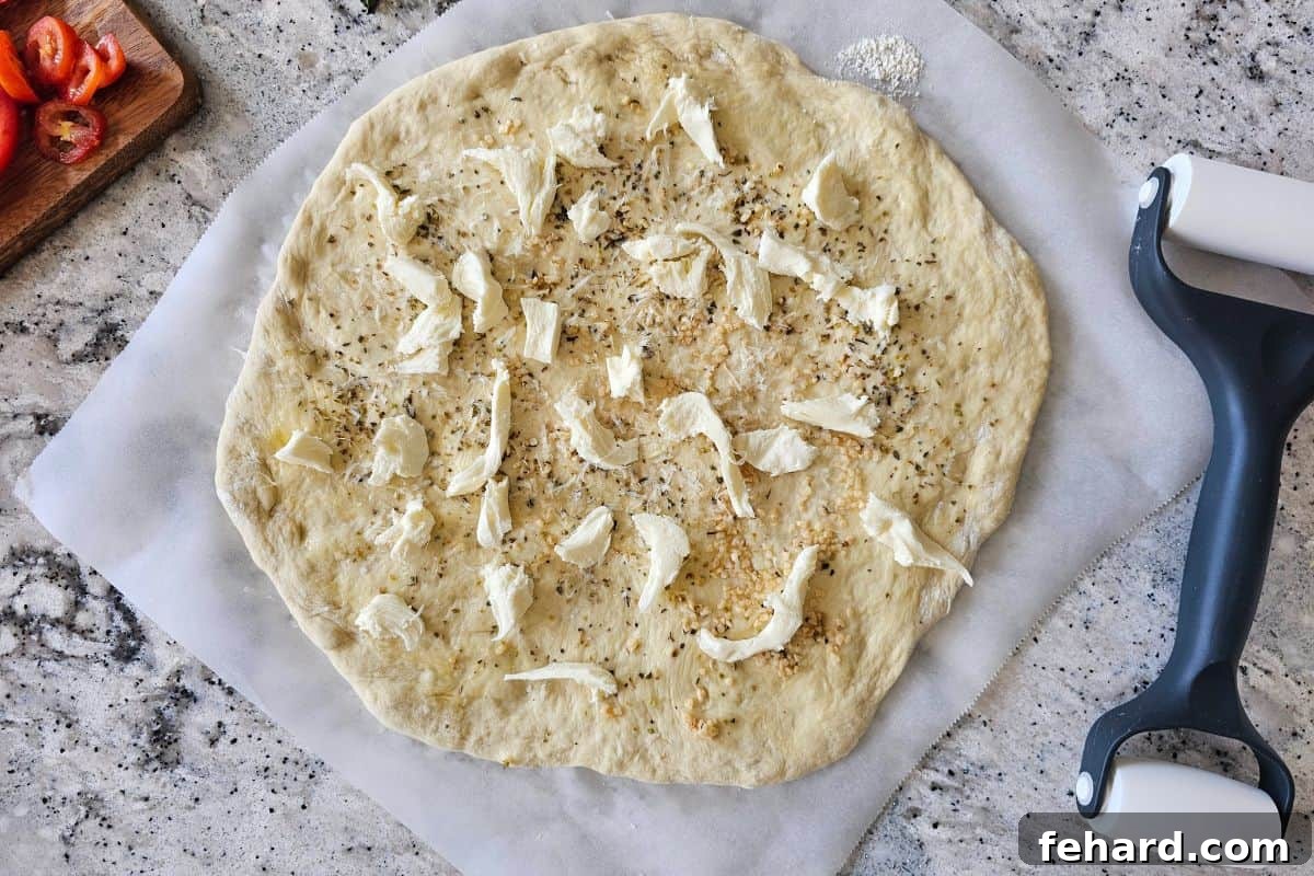 Pizza dough prepped with olive oil and seasonings, then topped with an initial layer of fresh mozzarella and Parmesan cheese.