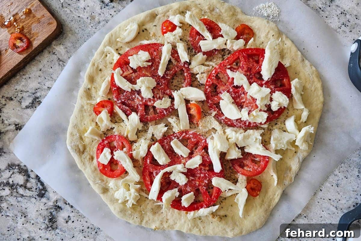 The pizza dough fully topped with layers of mozzarella cheese and fresh tomato slices, ready for baking.