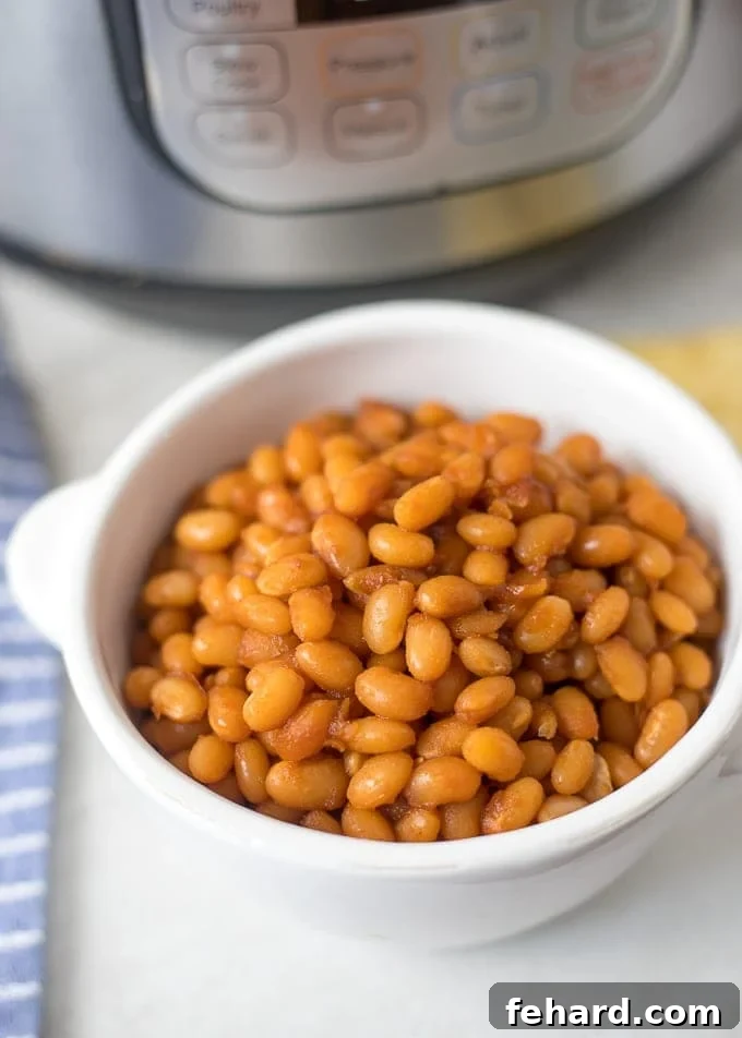 Instant Pot Baked Beans Recipe Baked Beans in a white serving dish next to an Instant Pot, showcasing the rich, dark sauce.
