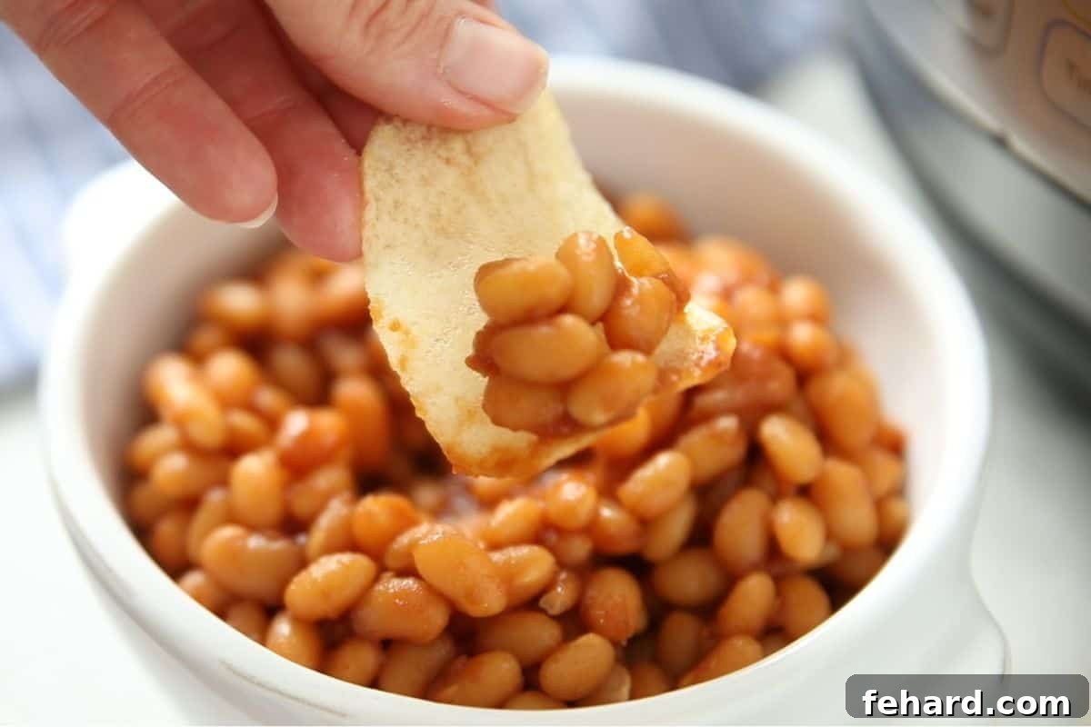 Recipe Baked Beans Instant Pot Serving A potato chip scooping up baked beans from a white bowl, illustrating a fun way to eat them.