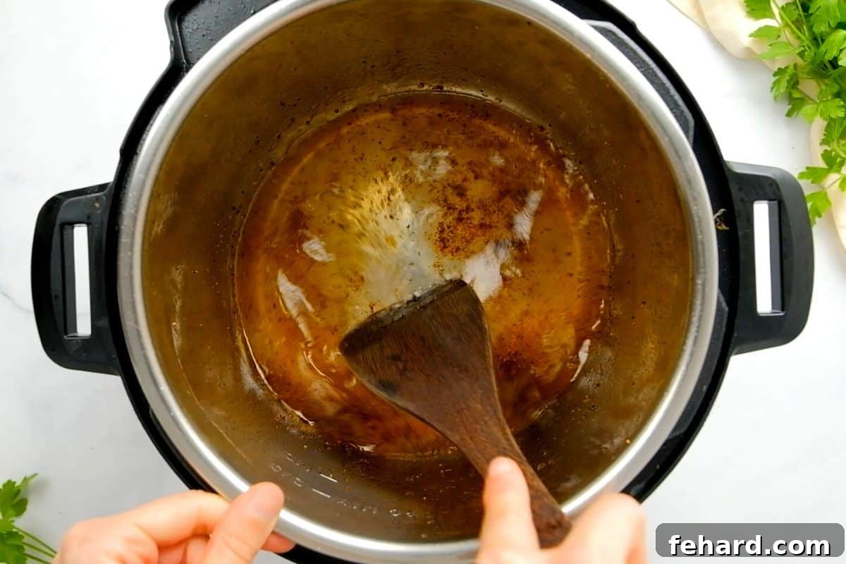 A wooden spoon efficiently scraping all the flavorful browned bits from the bottom of the Instant Pot's inner pot, a key step in deglazing after searing.