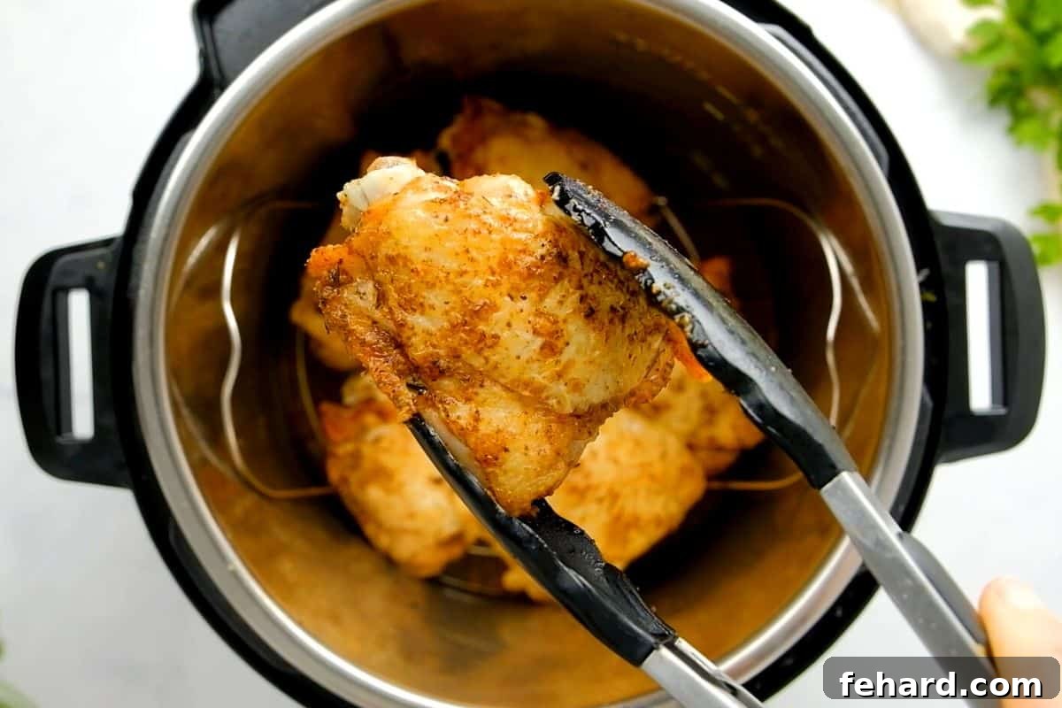 A pair of tongs gracefully lifting a perfectly cooked, golden-brown Instant Pot chicken thigh with a visibly crispy skin, while the pressure cooker rests in the background.
