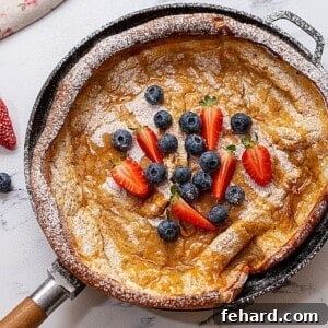 Fluffy, crispy German pancake in a cast iron skillet, elegantly topped with fresh berries and a hint of powdered sugar.