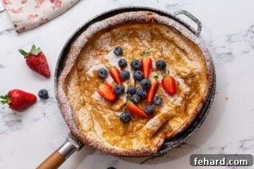 Baked Dutch oven pancake in skillet with berries and maple syrup, ready to eat.
