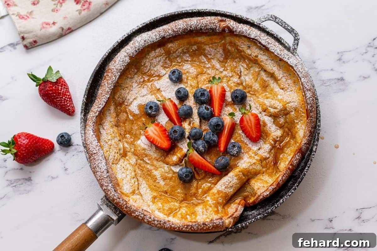 A freshly baked Dutch oven pancake in a skillet, beautifully garnished with vibrant mixed berries and a pour of golden maple syrup, ready to be enjoyed.