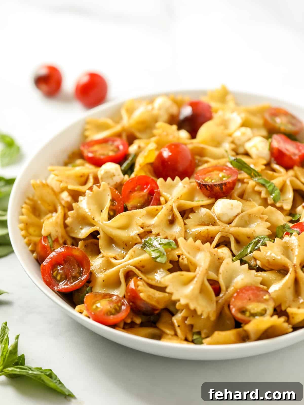 A large bowl of Caprese Pasta Salad, showcasing colorful tomatoes, white mozzarella, and green basil against a backdrop of pasta. Perfect for a summer gathering.