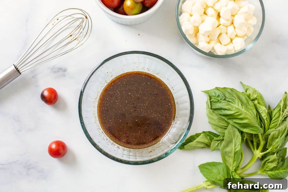 A small glass bowl filled with freshly whisked balsamic vinaigrette, ready to dress the Caprese Pasta Salad.