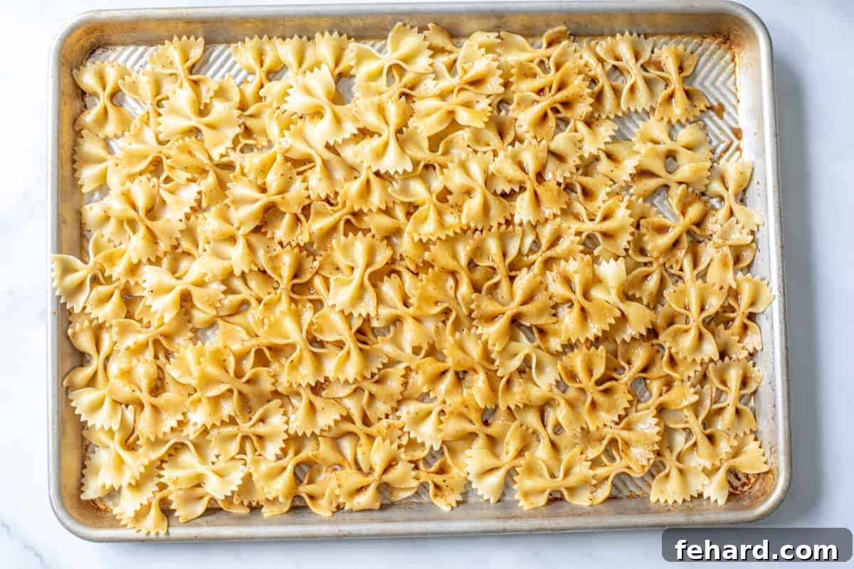 Warm, dressed pasta spread out on a sheet pan to cool, showing a light glaze of balsamic vinaigrette.
