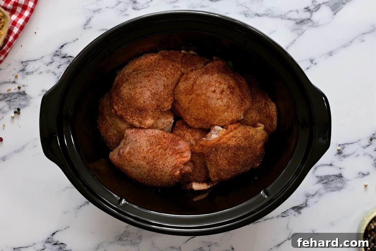 Easy BBQ Chicken Thighs Recipe: Slow Cooker Setup Seasoned raw chicken thighs arranged on a bed of sliced onions in a slow cooker.