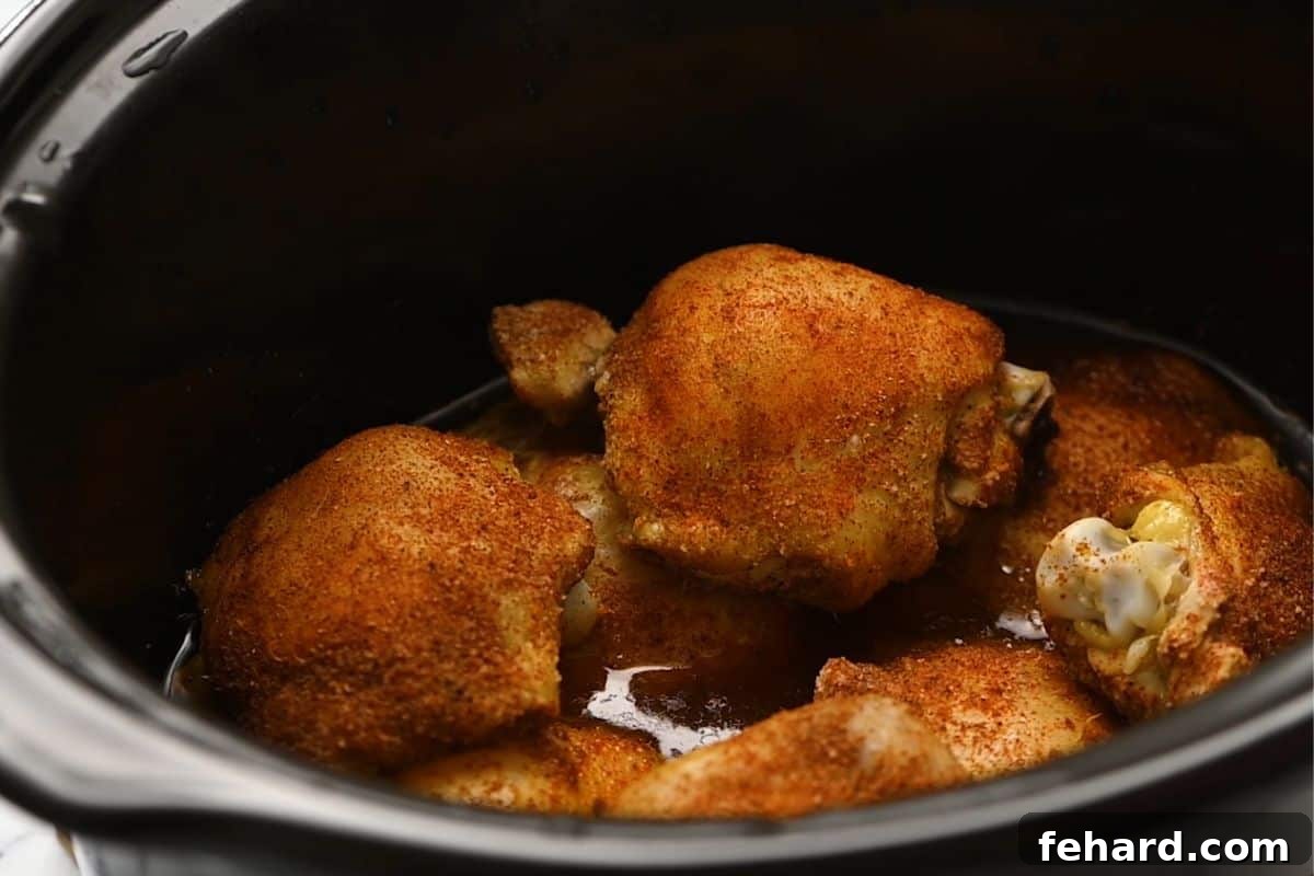 Slow Cooker Chicken Thighs Recipe: Cooking Cooked seasoned chicken thighs simmering in the slow cooker with juices.