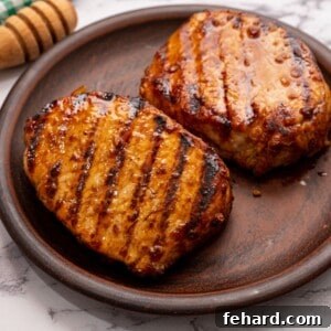 Grilled Pork Chops on wooden platter next to honey, ready to serve.