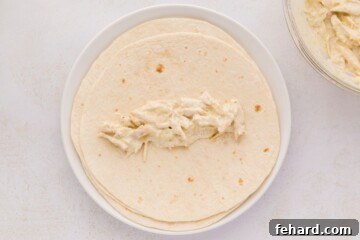 A soft flour tortilla being meticulously filled with a generous scoop of the creamy chicken mixture, poised for its transformation into a delectable enchilada.