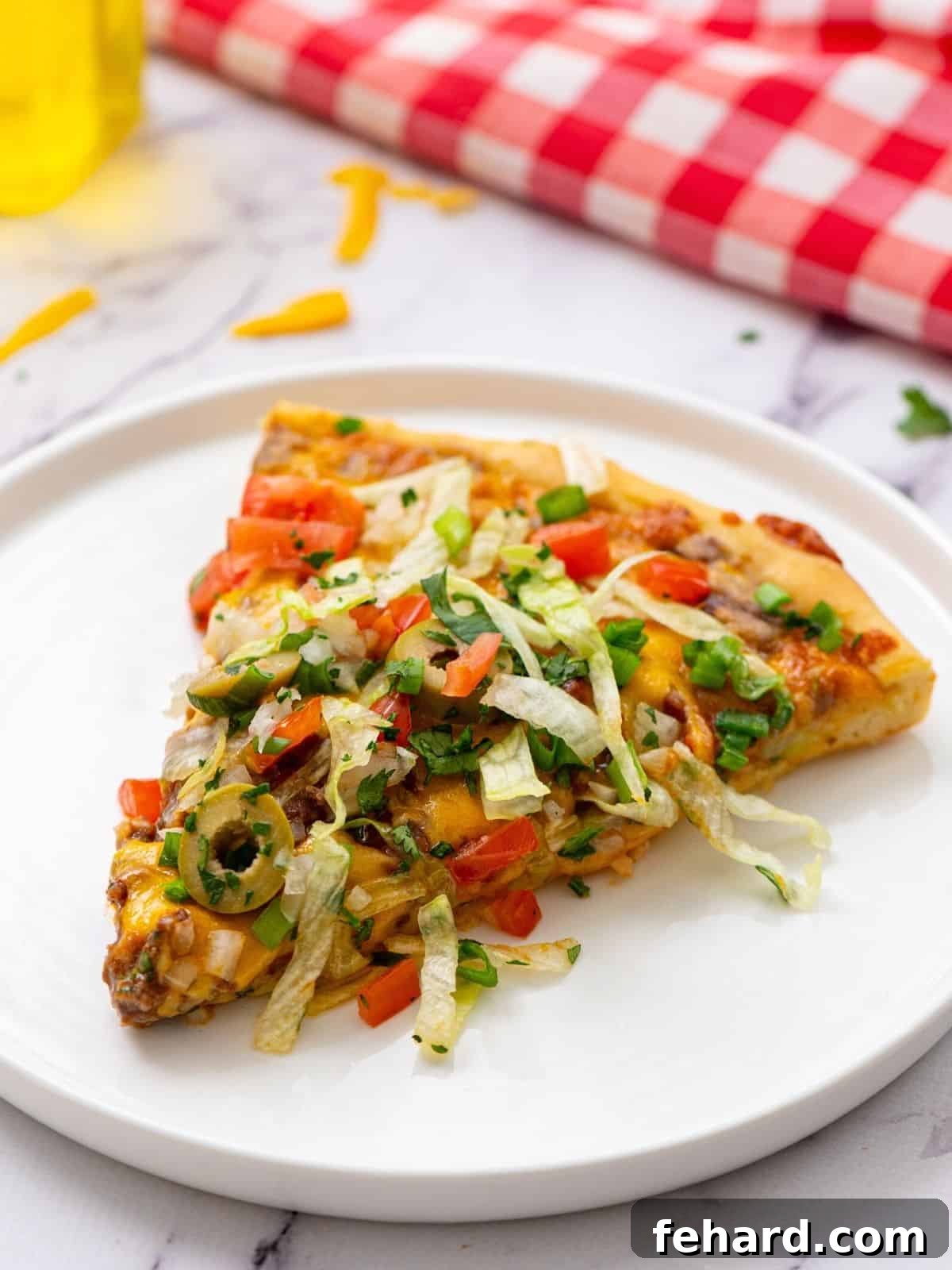 The Ultimate Homemade Taco Pizza Recipe A delectable slice of Taco Pizza, richly topped with fresh lettuce, diced tomatoes, and cilantro, served on a pristine white plate. The golden crust and vibrant toppings create an irresistible visual.